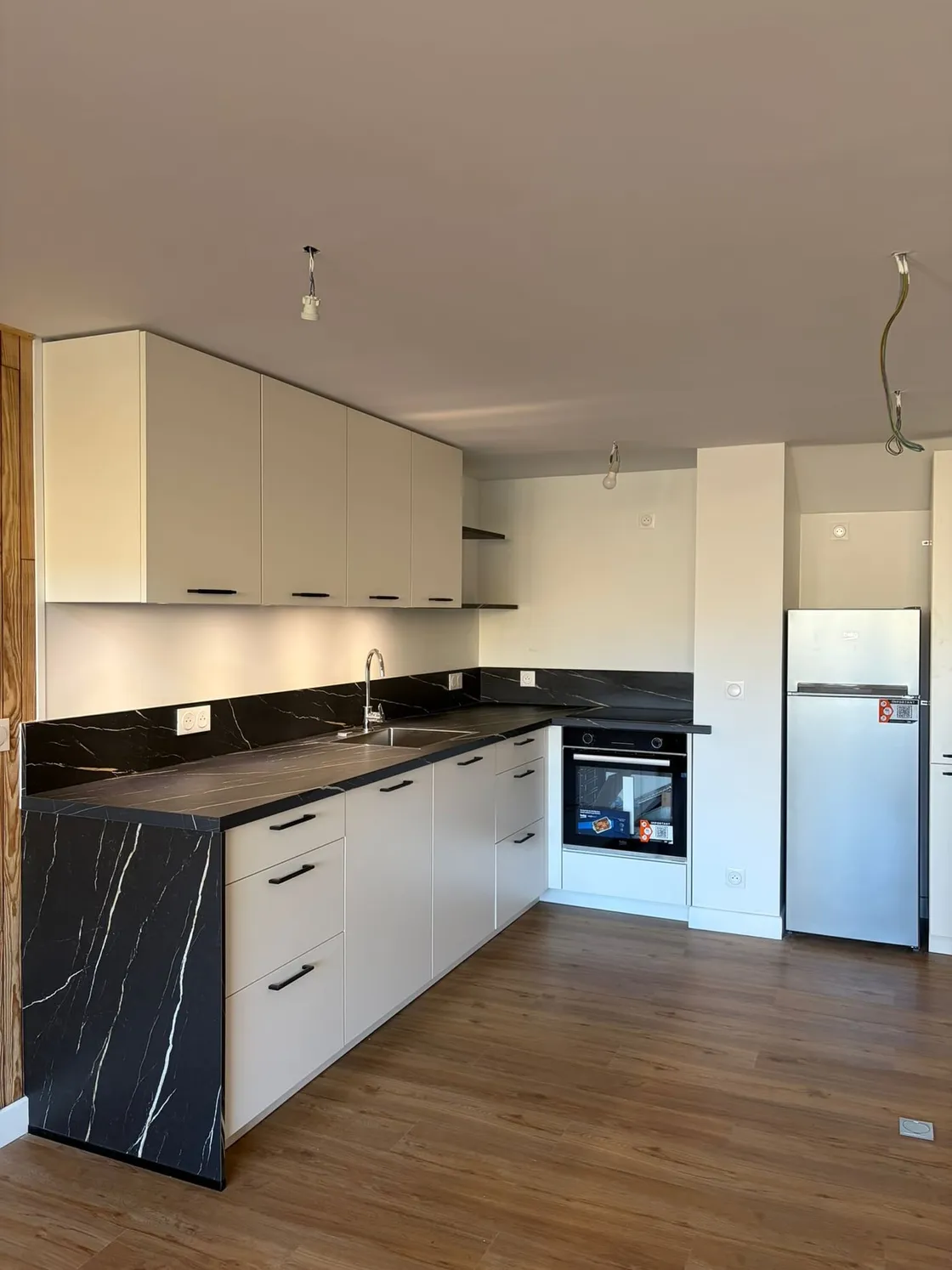 Cuisine sur mesure en L, façades sable sans poignée et plan de travail effet marbre noir